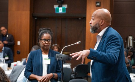 Optimized Alt Text: Close up portrait of Member of Parliament Michael Coteau delivering introductory remarks from a wooden legislative podium during the incorporation meeting.