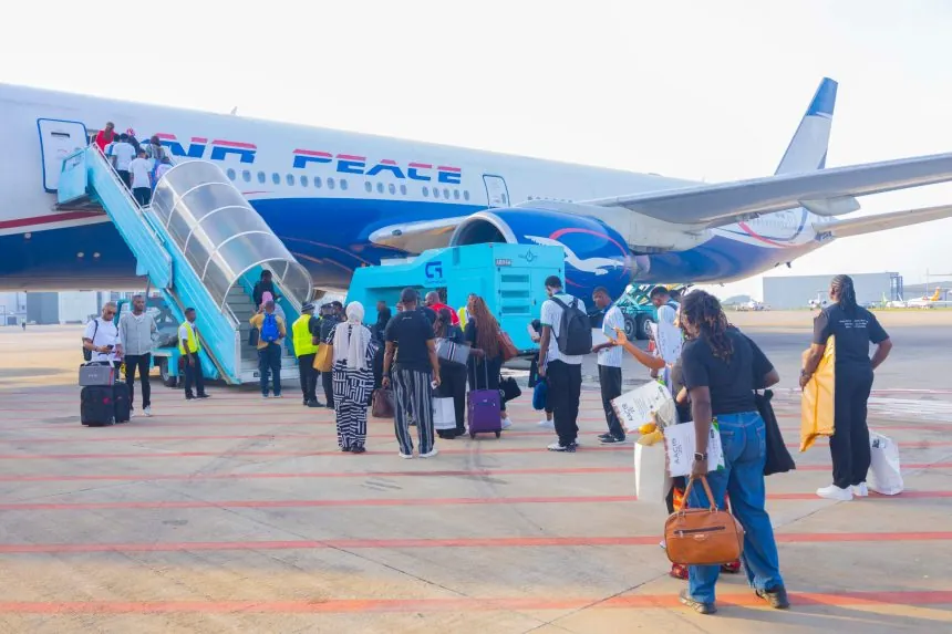 Nigerian travellers with luggage walking toward an Air Peace aircraft to board a flight.