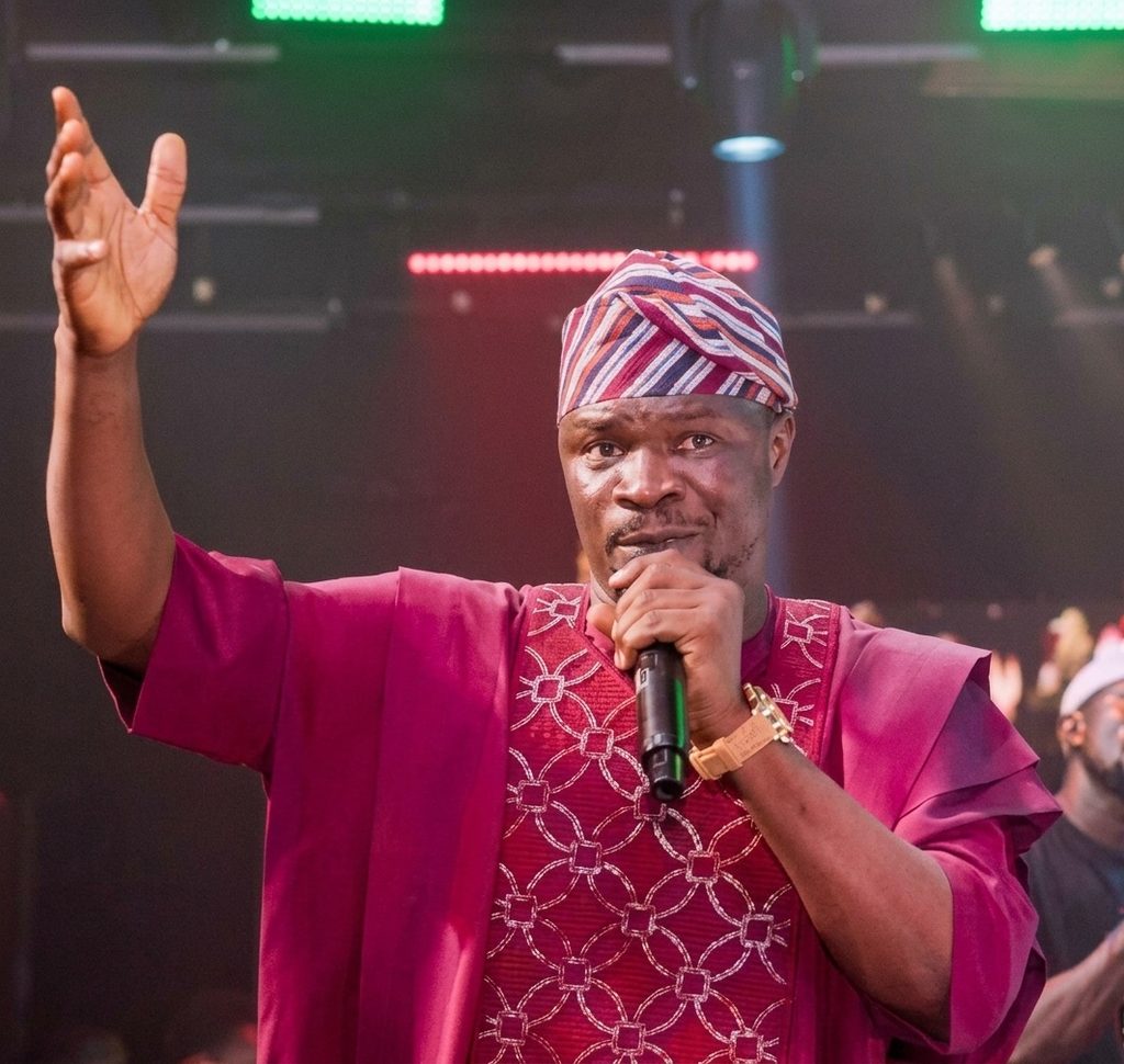 Toluwanisings performing gospel music at a microphone during a live praise session.